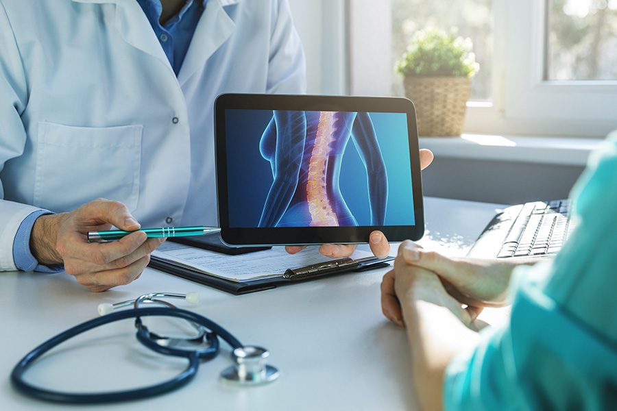 Employee Benefits - Close of a Doctor Holding a Tablet Showing the Results of a X-Ray to a Patient at His Desk in His Office