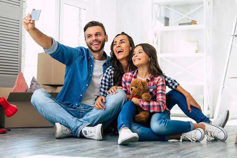 Personal Insurance - A Young Family of a Father, Mother and Daughter Sitting on the Floor of Their New Home Taking a Selfie and Laughing Together