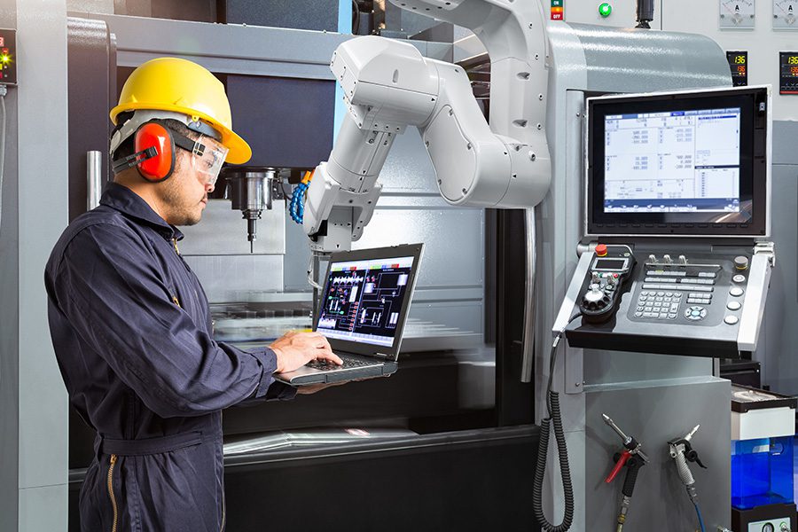 Specialized Business Insurance - A Maintenance Engineer is Using a Laptop to Control an Automatic Robotic Hand in a Smart Factory